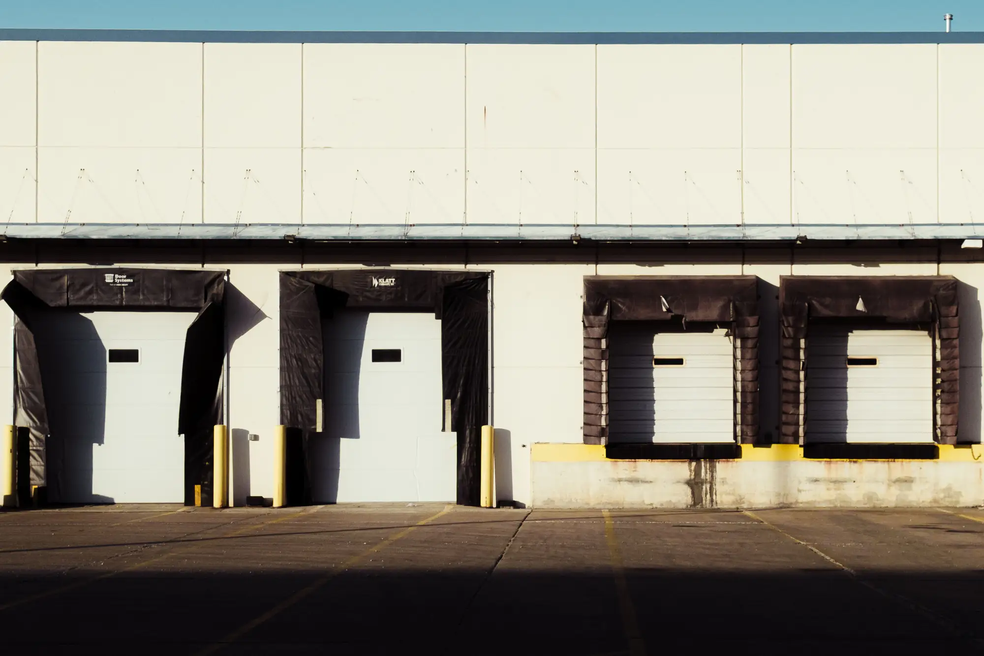 Closed dock doors along the back wall of a plant, with an empty truck apron in front